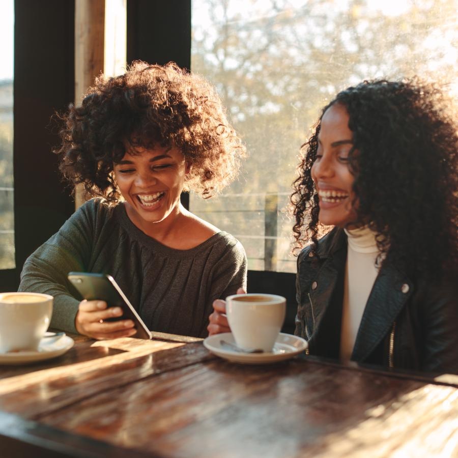 a couple of women sitting at a table with coffee and a phone